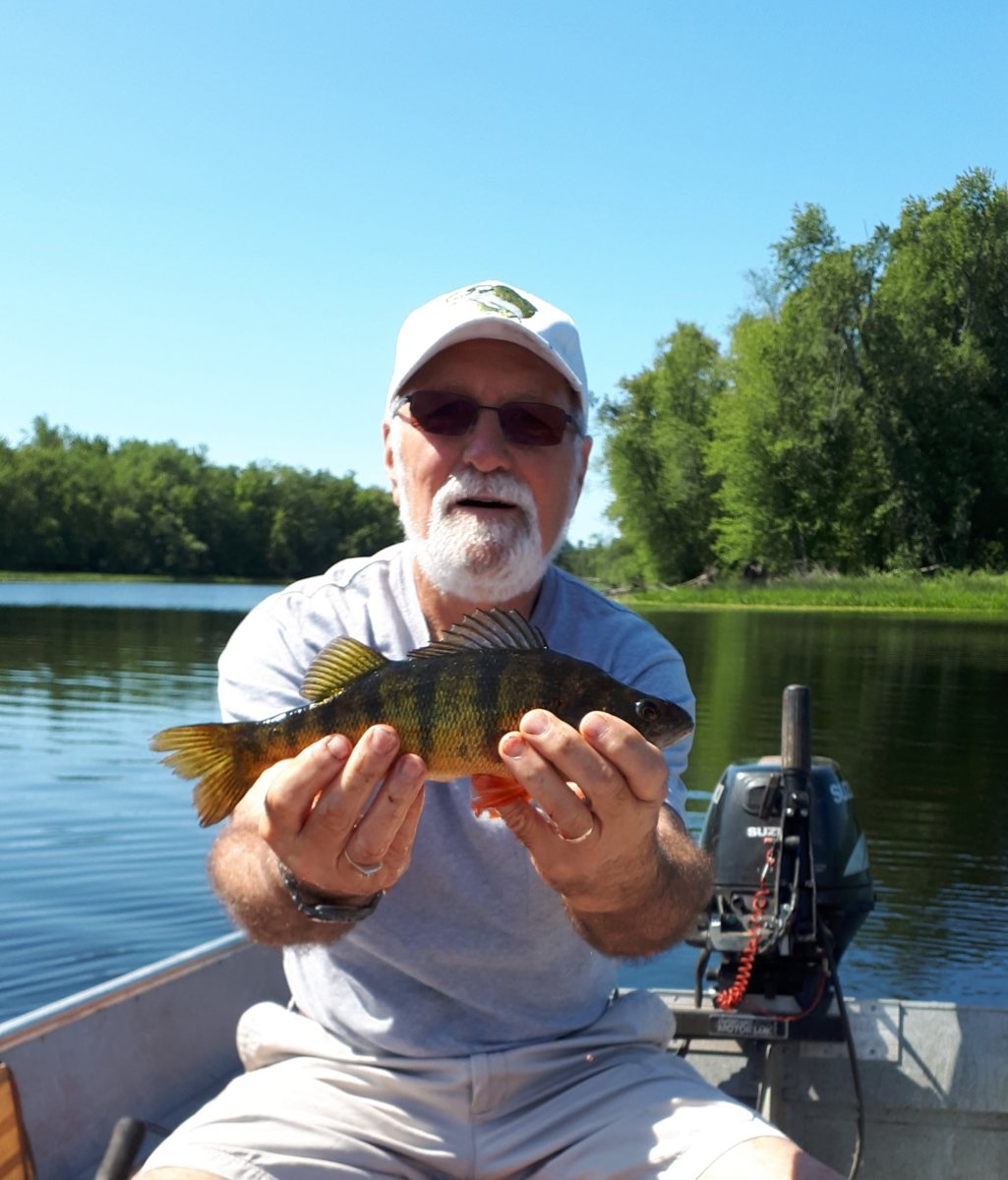 Dennis in a fishing boat holding up a yellow perch