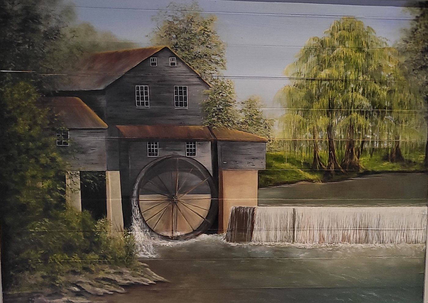 Painting on wooden planks of an old grist mill with a water wheel beside a weir